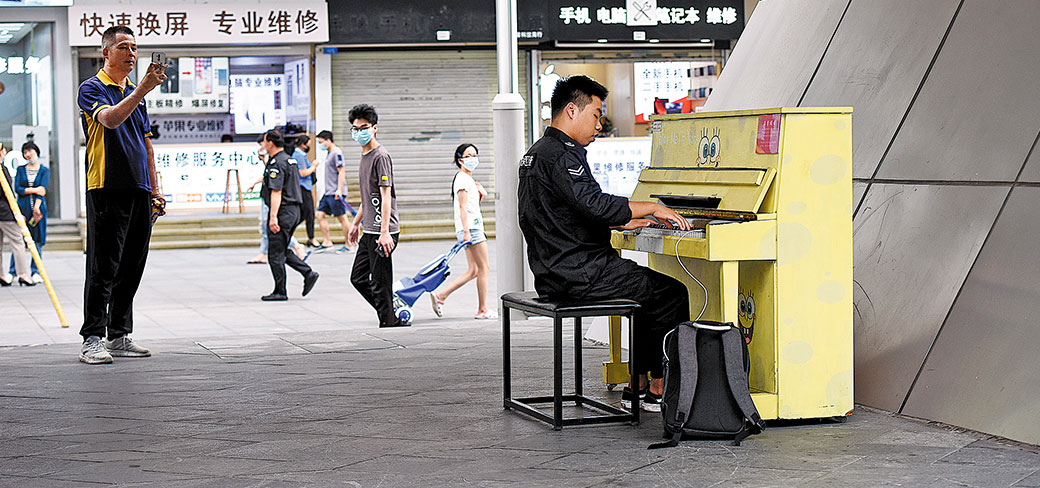 Un agent de sécurité au clavier d’un piano placé sous les escaliers mécaniques du Huaqiangbei à Shenzhen, dans la province du Guangdong. YI YANG / FOR CHINA DAILY