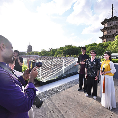 Un touriste étranger (au centre) prend une photo avec des artistes du Nanyin de Quanzhou sur le site pittoresque de la rue de l'Ouest à Quanzhou, dans la province du Fujian (sud-est de la Chine), le 20 juin 2025. (Xinhua/Jiang Kehong)